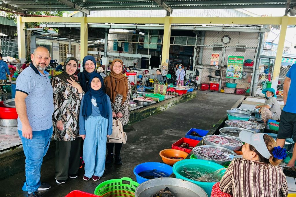 다양한 색상의 바구니와 컨테이너를 둘러싼 야외 시장에서 포즈를 취하고 있는 5명의 그룹.