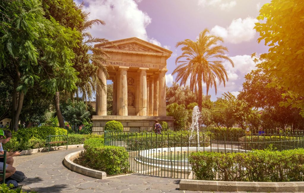 야자수가 우거진 나무와 돌길, 햇살이 내리쬐는 정원의 작은 울타리 분수로 둘러싸인 고대의 사원.