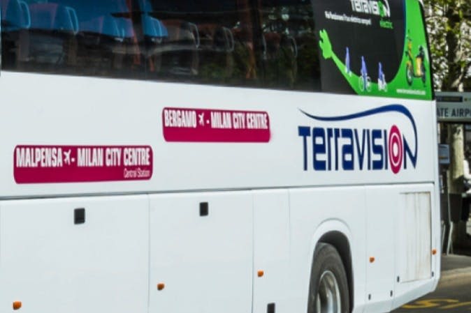 "Terravision" 과 "Bergamo to Milan City Centre" 표지판이 있는 흰색 버스의 측면 모습으로 바퀴의 일부를 보여줍니다.