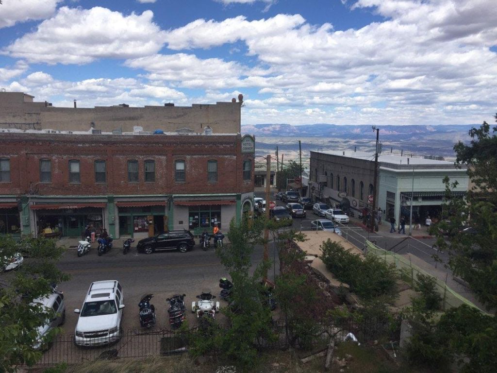 주차된 오토바이, 자동차, 산책하는 사람들이 있는 작은 마을 거리. 벽돌 건물과 경치 좋은 풍경을 배경으로.