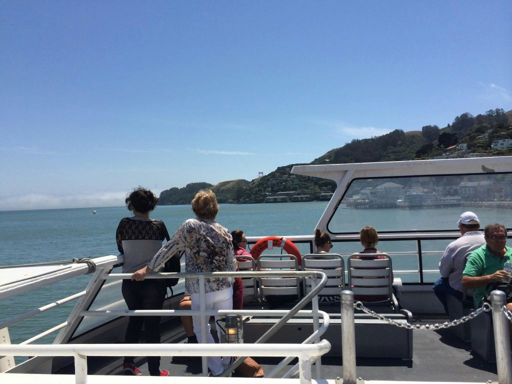 사람들은 보트 갑판에 서서 맑고 푸른 하늘 아래에서 물의 경치와 먼 해안선을 즐기고 있습니다.