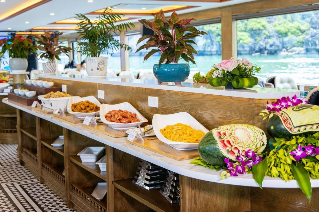 다양한 요리와 장식용 화분, 새겨진 수박이 놓인 뷔페 테이블은 경치 좋은 창문 전망을 자랑하는 조명이 좋은 식사 공간에 마련되어 있습니다.