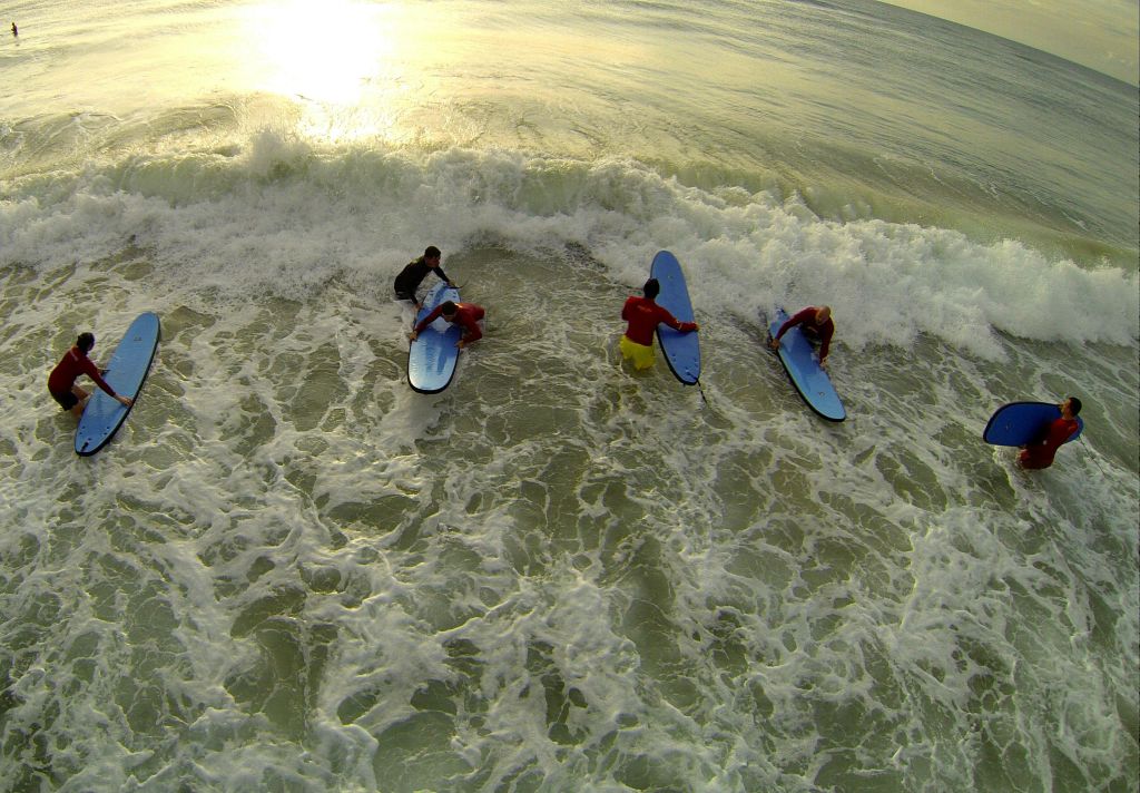 해가 지는 동안 해안 근처에서 파도를 헤치며 바다에서 푸른 서핑 보드를 타는 세 사람.
