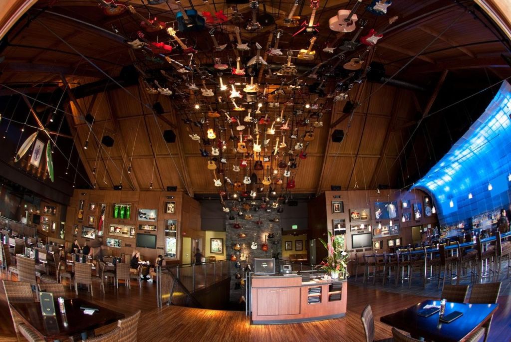 나무 천장과 테이블과 진열 케이스로 둘러싸인 수많은 기타가 걸려 있는 레스토랑 인테리어.