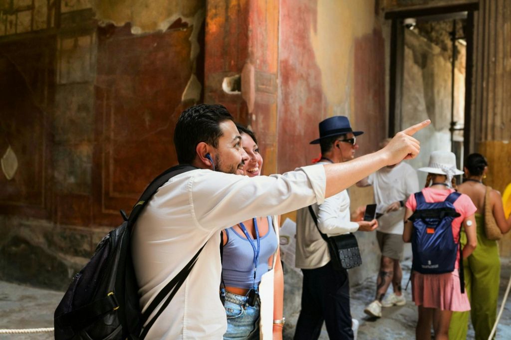 고풍스럽고 화려한 벽을 배경으로 실내에서 셀카를 찍으며 미소를 짓는 남성과 여성. 다른 사람들은 배경에 있습니다.