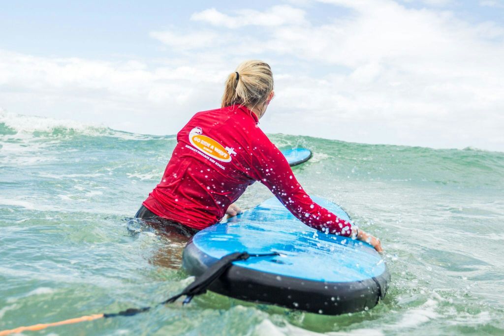 파도와 흐린 하늘을 배경으로 바다에서 파란색 서핑 보드를 들고 있는 빨간색 셔츠를 입은 사람.
