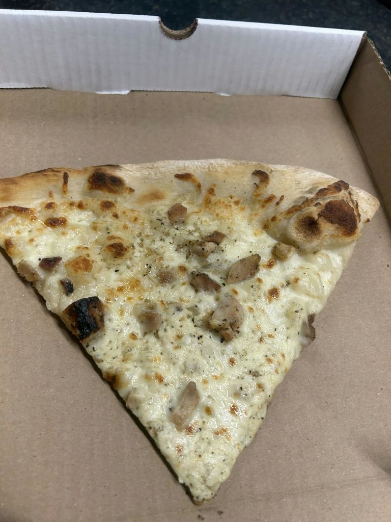 갈색 판지 포장에 구운 치킨 조각이 담긴 흰색 피자 한 조각.