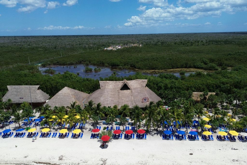 숲과 강을 배경으로 초가 지붕, 화려한 우산, 일광욕 의자가 있는 해변 리조트의 공중 전망.