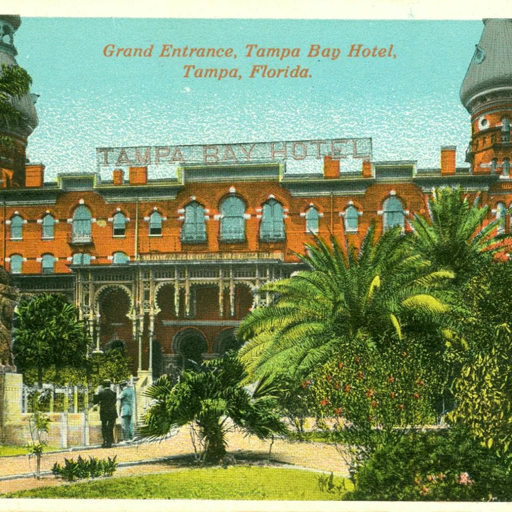 야자수로 둘러싸인 '탬파베이 호텔' 이라는 이름의 붉은 벽돌 건물. 풍경이 아름다운 정원에서 두 사람이 길을 걷고 있습니다.