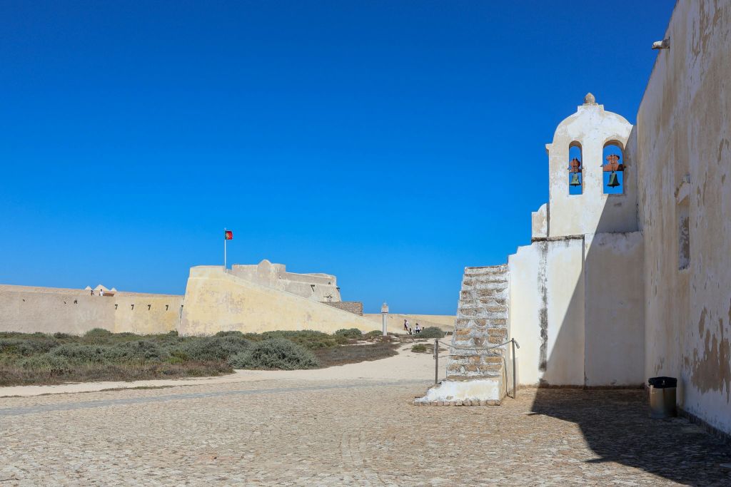 맑고 푸른 하늘 아래 석조 요새 옆에 종탑이 있는 작은 흰색 예배당.