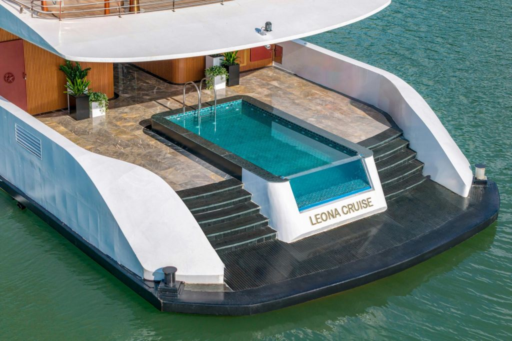 대리석 타일과 물가로 이어지는 계단이 있는 요트 위의 옥상 수영장. 측면에 "레오나 크루즈" 라는 이름이 표시됩니다.