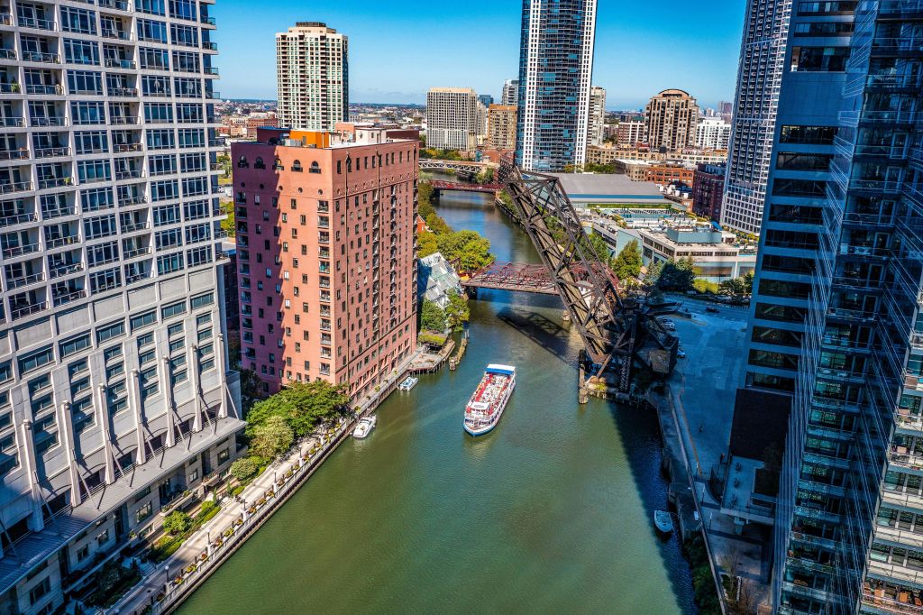 높은 건물과 높이 솟은 도개교로 둘러싸인 흰색과 빨간색 보트가 있는 도시를 가로지르는 강.