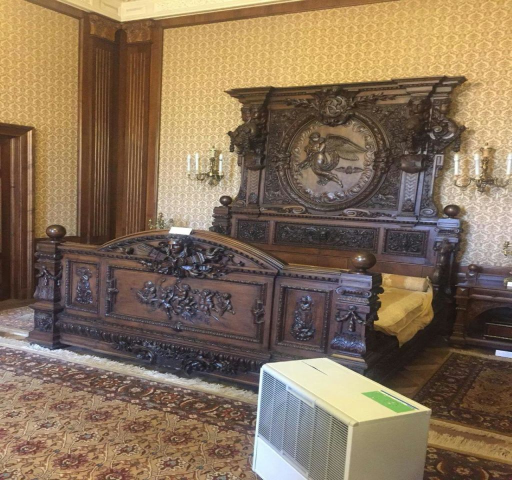 무늬가 있는 벽지, 페르시아산 러그, 공기청정기가 있는 객실에 정교한 디자인으로 장식된 나무 침대가 있습니다.