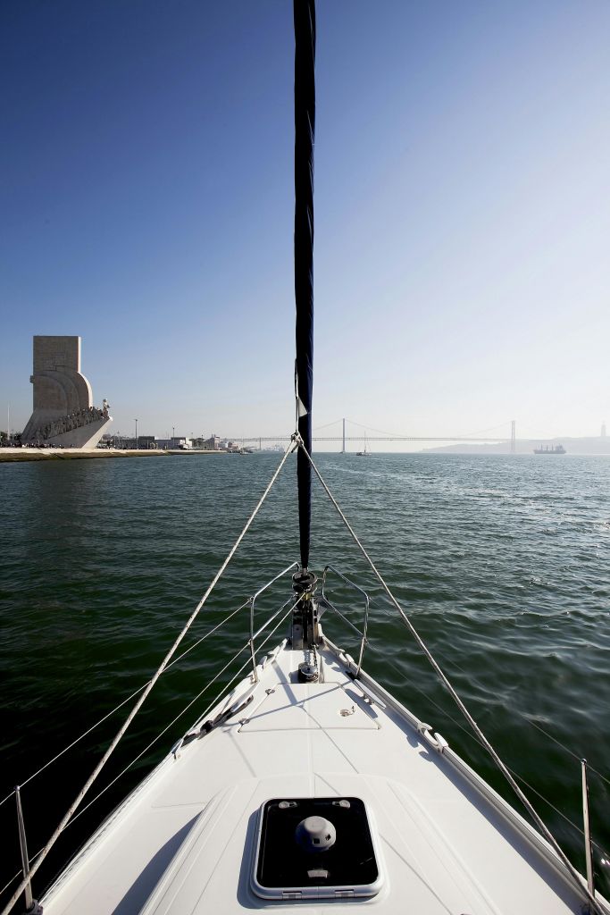 왼쪽에 기념비가 있고, 현수교가 배경에 있으며, 맑은 하늘 아래 광활한 물이 있는 범선의 활에서 바라보는 풍경.