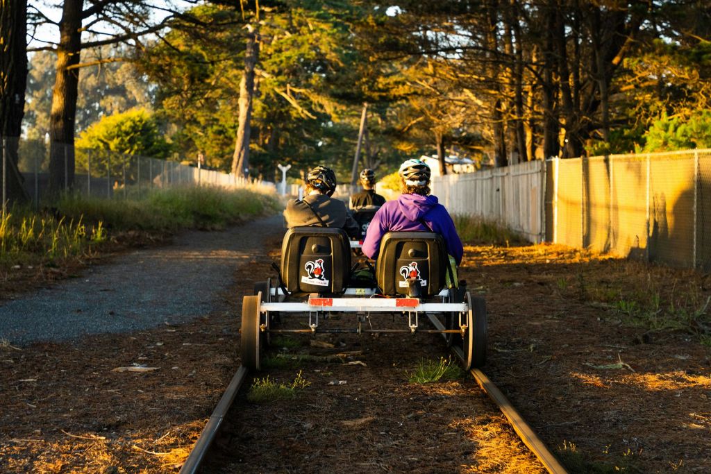 헬멧을 쓴 두 사람이 나무로 둘러싸인 트랙에서 철도 차량을 타고 숲이 우거진 곳에서 울타리를 치고 있습니다.
