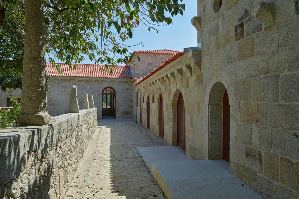 붉은 기와 지붕, 아치형 출입구, 옆으로 난 돌 통로, 머리 위로 나뭇가지가 있는 석조 건물.