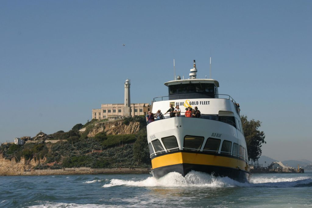 "Blue & Gold Fleet" 이라는 이름의 페리가 탑승객과 함께 접근하고 있습니다. Alcatraz Island 등대가 배경에 있습니다.