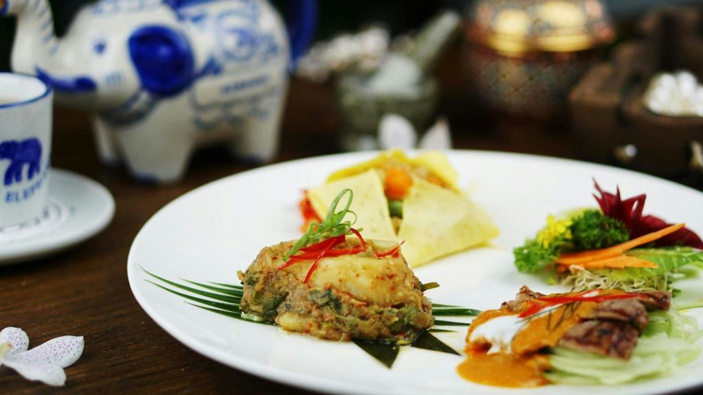 칠리 슬라이스와 파를 배경으로 장식된 찐 어묵을 포함한 다양한 태국 요리가 담긴 접시입니다.