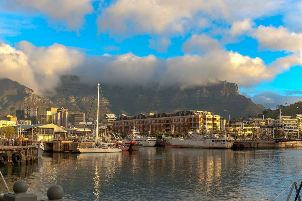 잔잔한 물에 배가 정박한 항구, 붉은 벽돌 건물, 부분적으로 구름으로 뒤덮인 산.