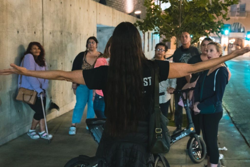 두 팔을 활짝 벌려 이야기를 들려주는 가이드가 인파 앞에 서 있습니다.