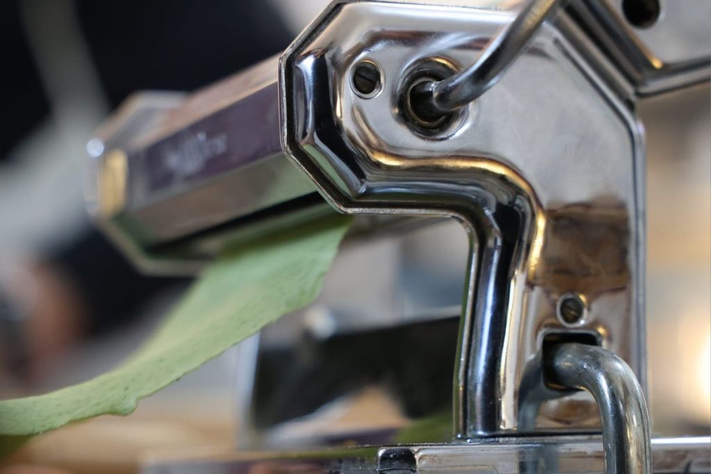 초록색 파스타 반죽이 굴러다니는 금속 파스타 메이커의 클로즈업입니다.