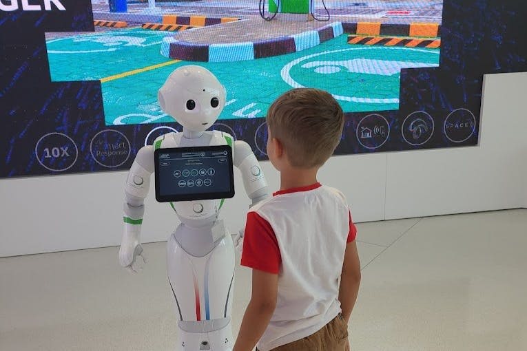 다채로운 장면을 보여주는 대형 스크린 앞에서 휴머노이드 로봇이 아이와 상호 작용합니다.