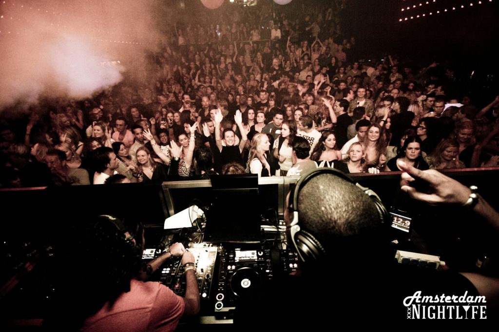 헤드폰을 착용한 DJ가 나이트클럽에서 활기차고 활기찬 공연을 펼칩니다. 본문에는 "암스테르담 나이트리페" 라고 적혀 있습니다.