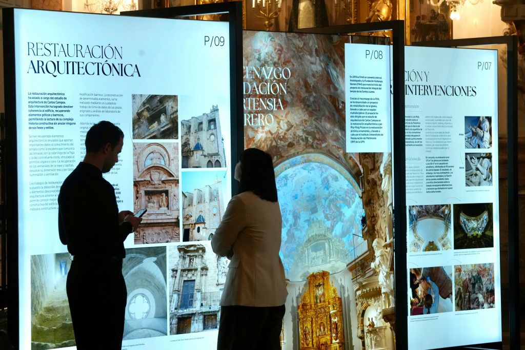 전시 환경에서 건축 이미지와 텍스트를 보여주는 조명 디스플레이 패널 앞에 두 사람이 서 있습니다.