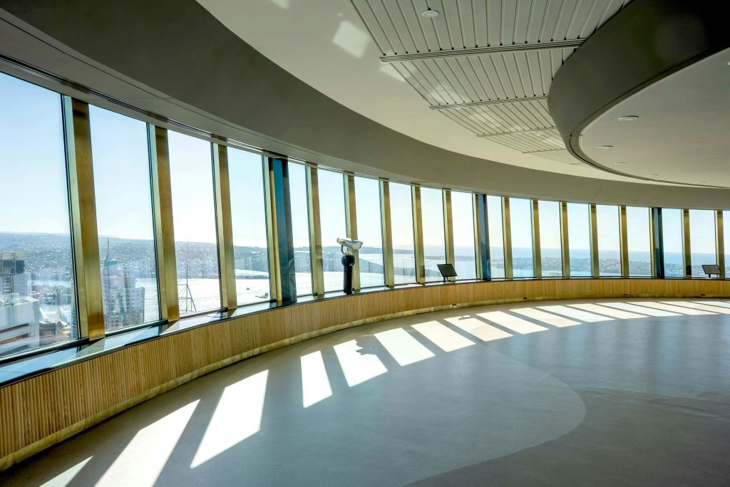 커다란 창문, 전망용 망원경, 해안가 도시 풍경이 내려다보이는 의자 2개가 있는 밝은 전망대.