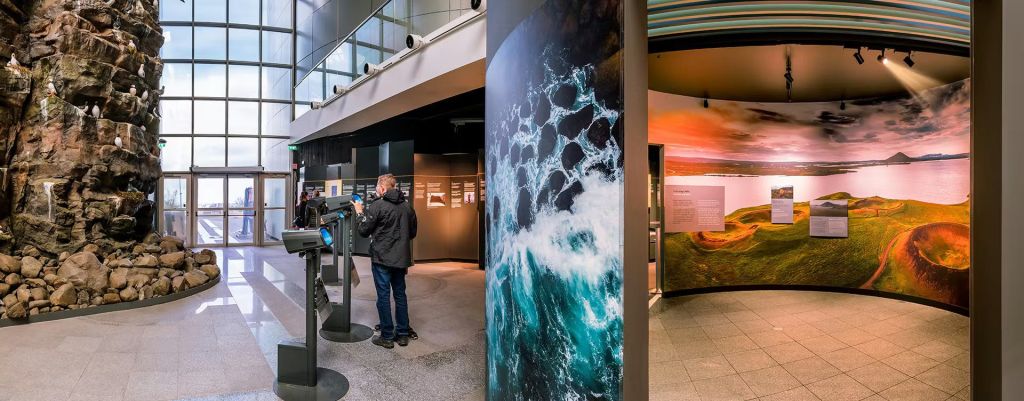정보 패널, 대형 바다 물결 사진, 디스플레이 화면과 상호 작용하는 사람이 전시된 실내 박물관 전시관입니다.