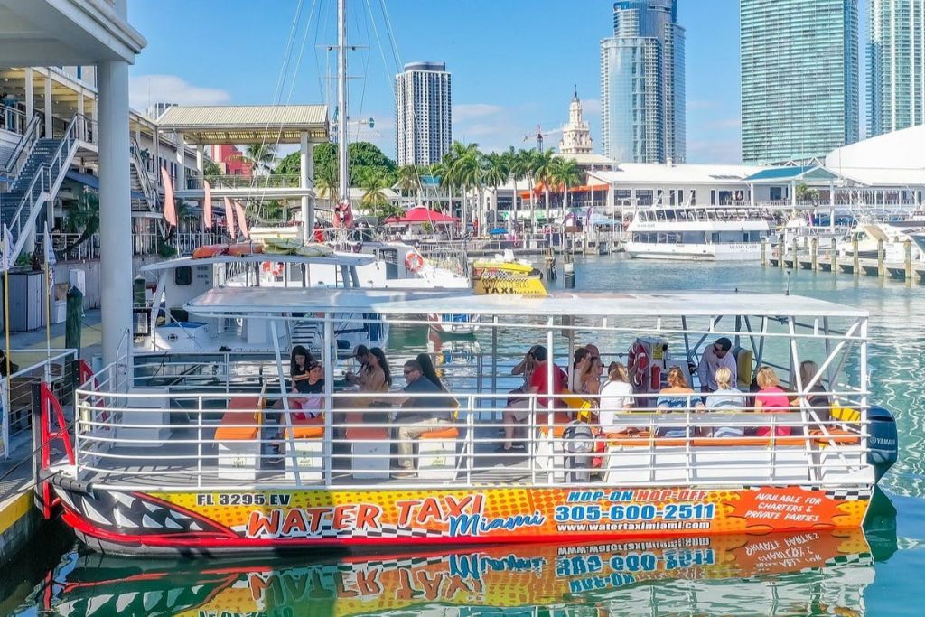 사람들은 높은 건물, 야자수, 기타 보트를 배경으로 정박지에서 수상 택시에 앉아 있습니다.