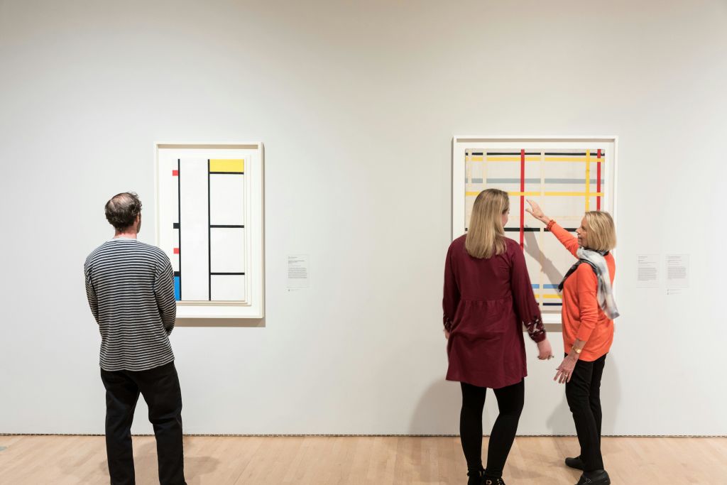 두 사람이 갤러리에서 흰색 벽에 액자 모양의 기하학적 그림이 그려진 추상 미술을 감상합니다.