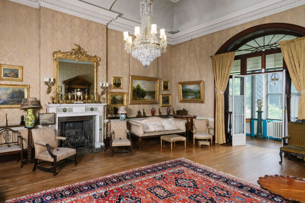 샹들리에가 있는 우아한 빈티지 거실, 벽난로 위의 화려한 거울, 앤티크 가구, 벽에 걸린 액자 예술 작품.