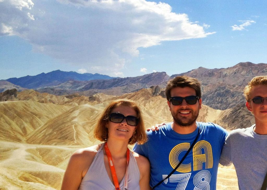 바위 언덕과 부분적으로 흐린 하늘이 있는 사막 풍경 앞에 선글라스를 쓴 두 사람이 서 있습니다.