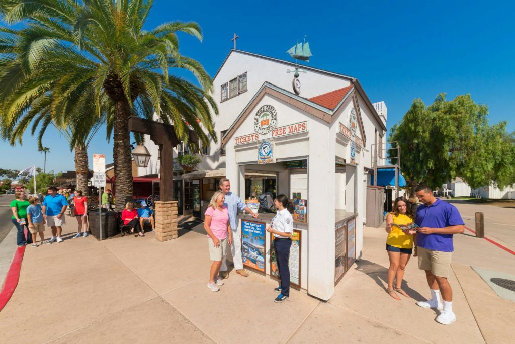 화창한 날 야외 티켓 부스와 안내 키오스크에서 나무와 건물을 배경으로 한 두 그룹의 사람들.