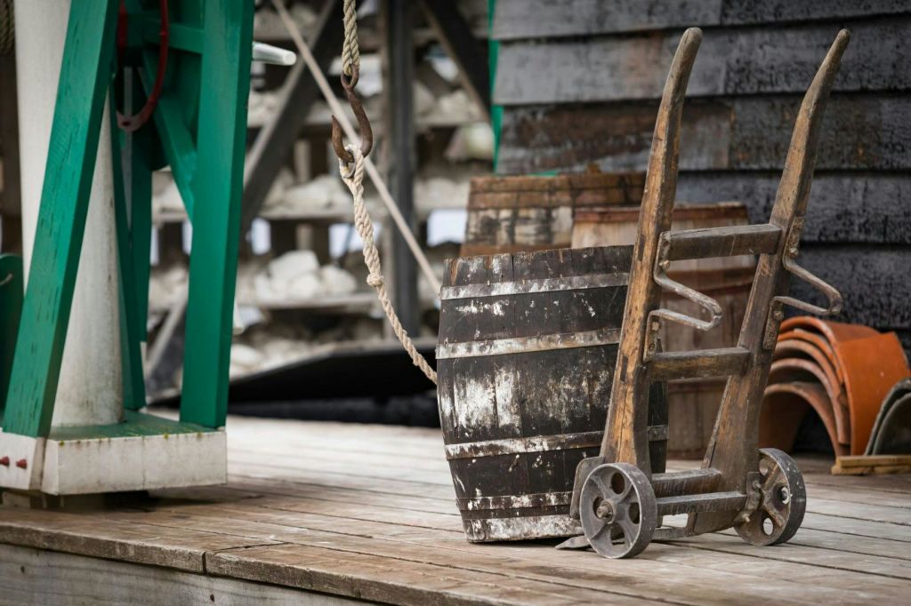 돌리에 달린 풍화된 나무 통이 나무 데크 위에 놓여 있으며, 밧줄과 녹색 금속 구조물이 함께 놓여 있습니다.