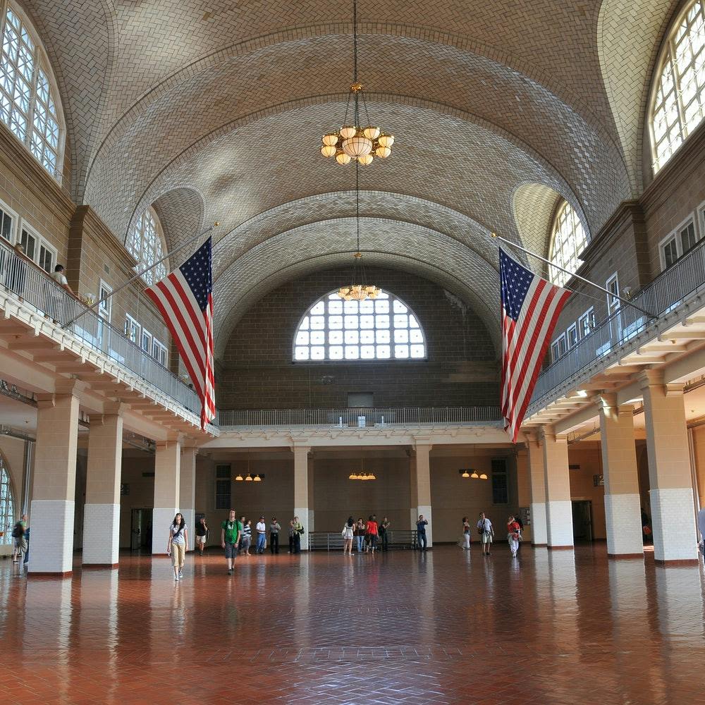 아치형 천장, 커다란 창문, 샹들리에, 미국 국기, 광택이 나는 바닥을 걷는 사람들이 있는 역사적인 홀.