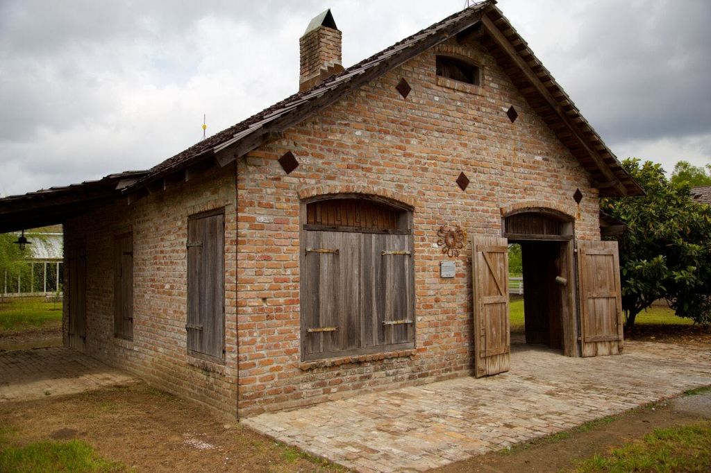 나무 셔터와 문이 있는 벽돌 건물로, 흐린 하늘 아래 굴뚝과 작은 복층 창문이 있습니다.