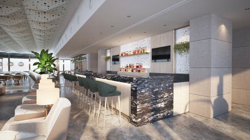 부드러운 조명 아래, 대리석 카운터, 녹색 바 스툴, 주류 병 선반, 벽에 두 개의 대형 스크린이 있는 현대적인 바.