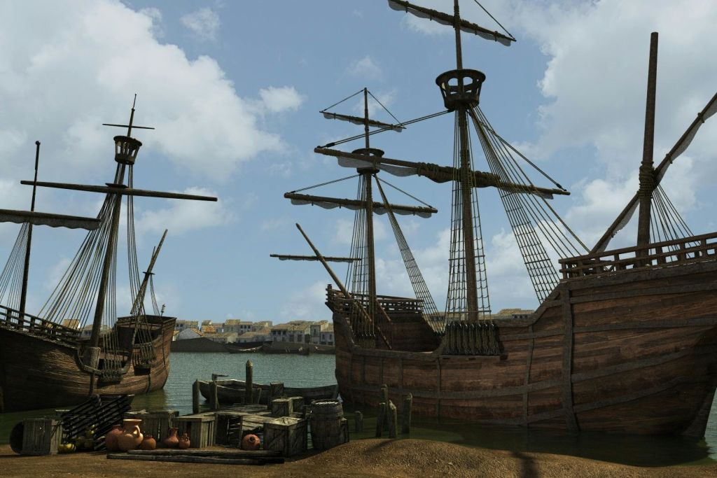 작은 부두와 상자가 있는 해안가에 정박한 두 척의 나무 항해선. 건물이 있는 마을이 배경으로 보입니다.