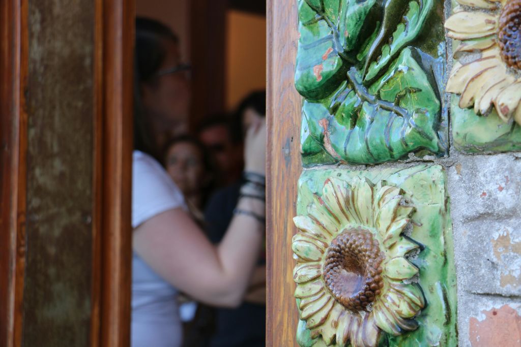 해바라기 디테일이 새겨진 도어 프레임의 클로즈업. 흰색 셔츠와 안경을 쓴 흐릿한 사람이 출입구를 통해 보입니다.