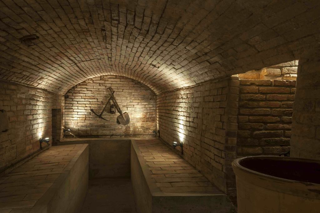 벽걸이 도구와 사이드 벤치가 있는 아치형 천장이 있는 희미한 벽돌 지하실입니다.