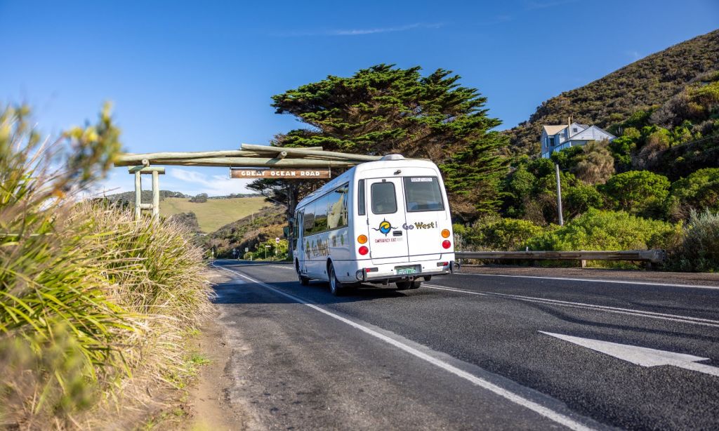 그레이트 오션 로드의 나무 아치 아래 나무와 언덕을 배경으로 'Go West!' 라는 이름의 투어 버스가 운행됩니다.