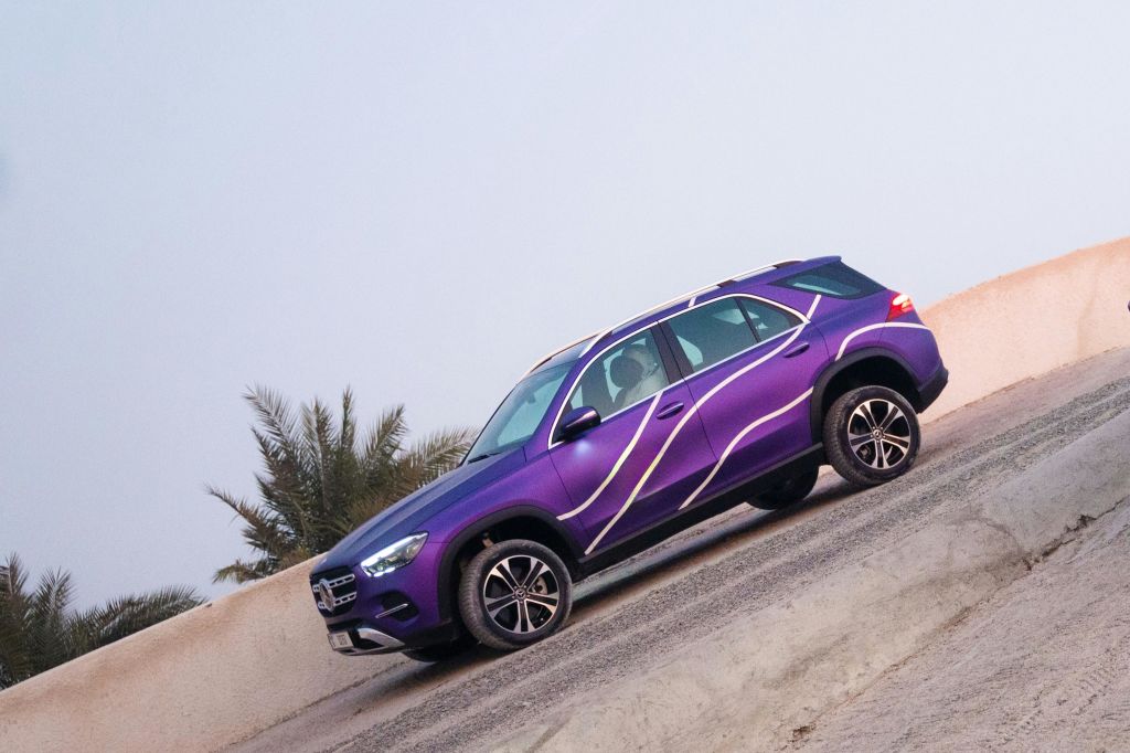 흰색 물결 모양의 라인이 있는 보라색 SUV가 장벽과 야자수를 배경으로 도로에 주차되어 있습니다.