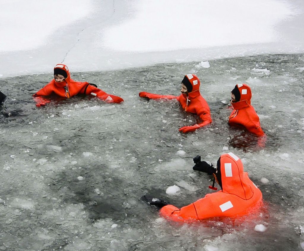 오렌지색 생존복을 입은 사람들은 부분적으로 얼어붙은 물에서 얼음물 구조를 연습합니다.