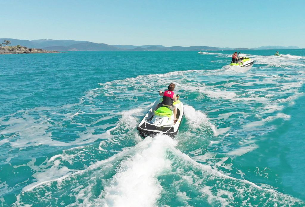 제트 스키를 탄 두 사람이 맑고 청록색 바다를 가로지르며 파란 하늘 아래에서 하얀 기상을 즐기고 있습니다.