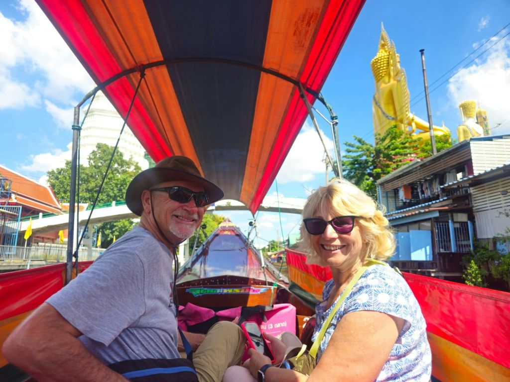 커다란 황금 조각상과 건물을 배경으로 화려한 타포린이 깔린 보트에 앉아 있는 남녀의 모습입니다.