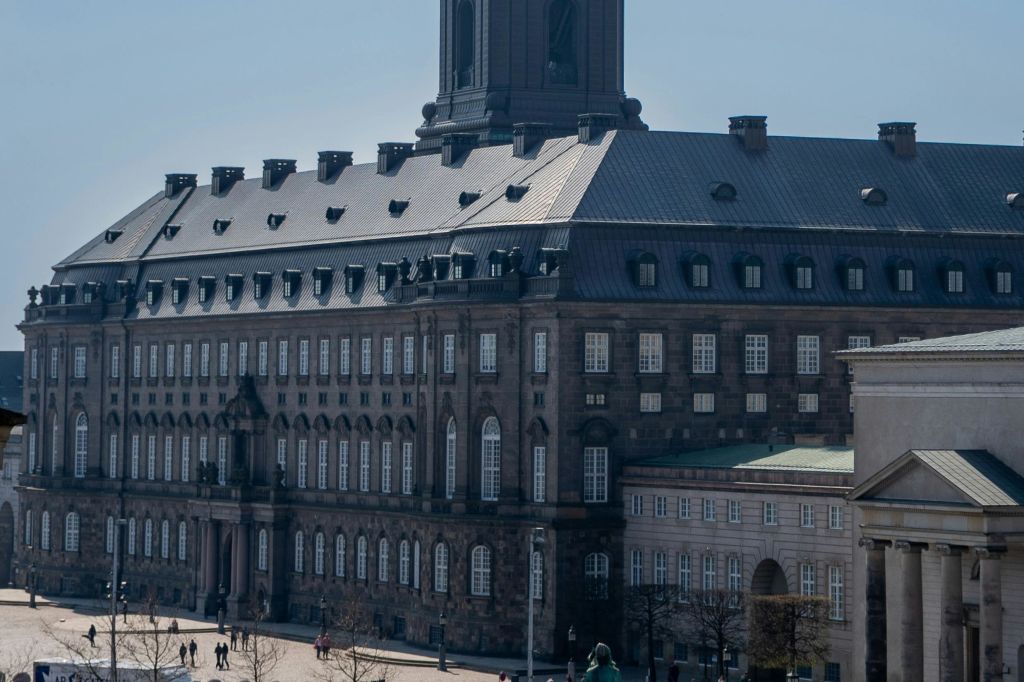 수많은 창문과 높은 시계탑이 있는 크고 유서 깊은 건물로, 사람들은 아래 넓은 마당에서 걷고 모입니다.