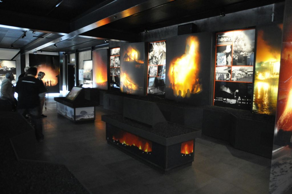 어두운 벽에 전시된 화재 이미지와 역사적인 사진이 있는 여러 패널이 있는 희미한 조명의 박물관 전시물입니다.