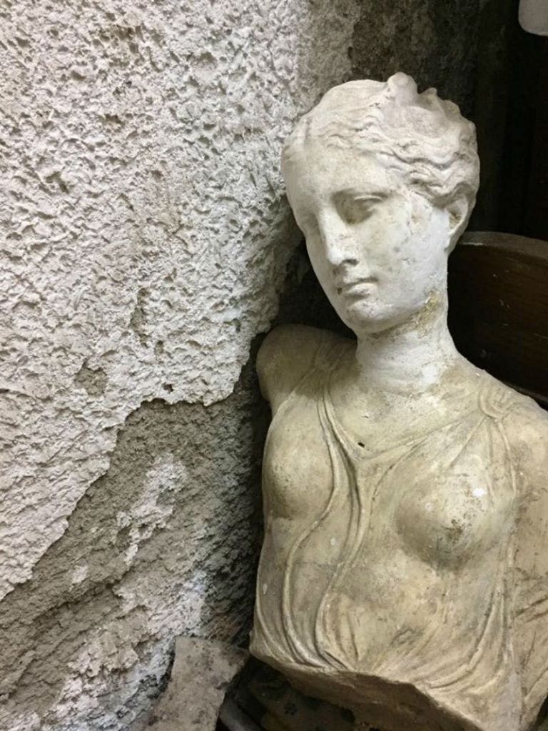 껍질이 벗겨진 질감의 벽에 기댄 풍화되고 고전적인 스타일의 흉상. 동상은 고요하고 쇠락한 시선을 받고 있습니다.